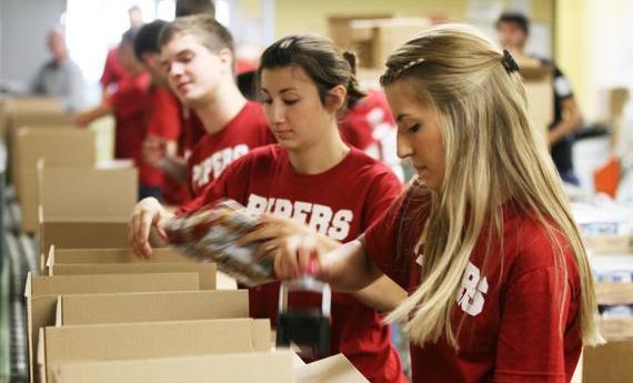 Three 51 student wearing red "PIPERS" shirts taping cardboard boxes while volunteering