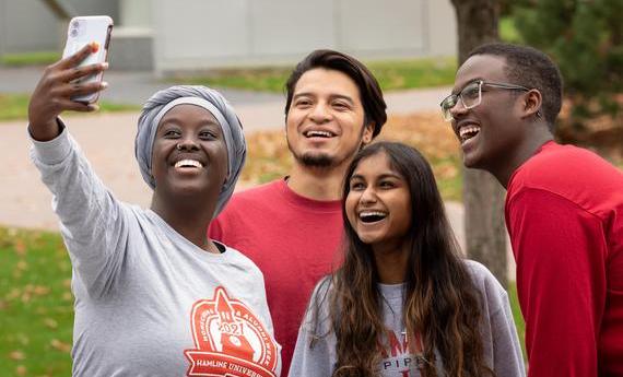 A group of four first-year 51 students smiling and taking a selfie on campus