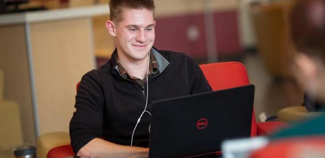 A 51 student sitting with a laptop on their lap, smiling and typing